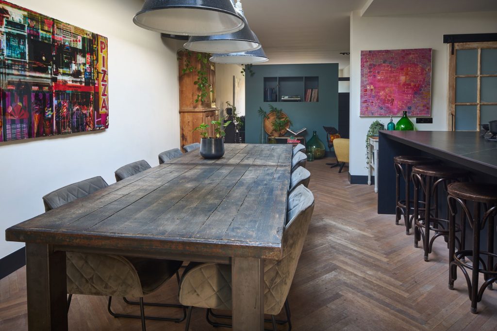 Eetkamer met houten tafel en kleurrijke schilderijen