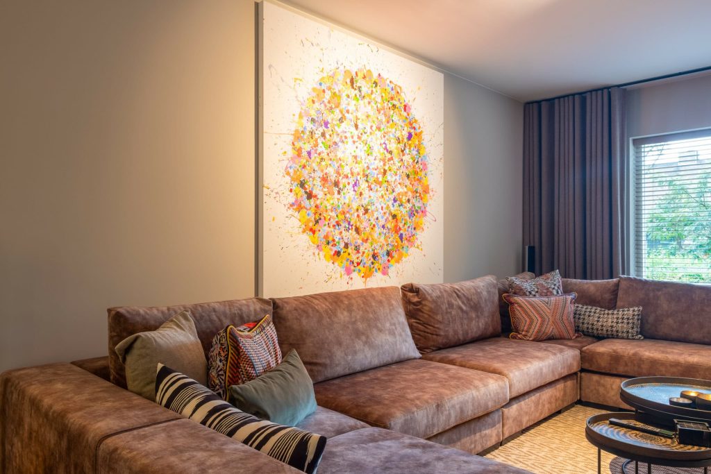 Moderne woonkamer met kleurrijk schilderij boven bruine bank.