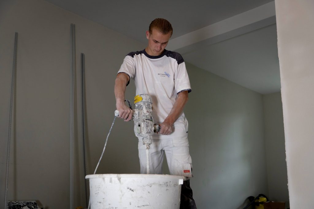 Man mengt verf in bouwemmer met machine